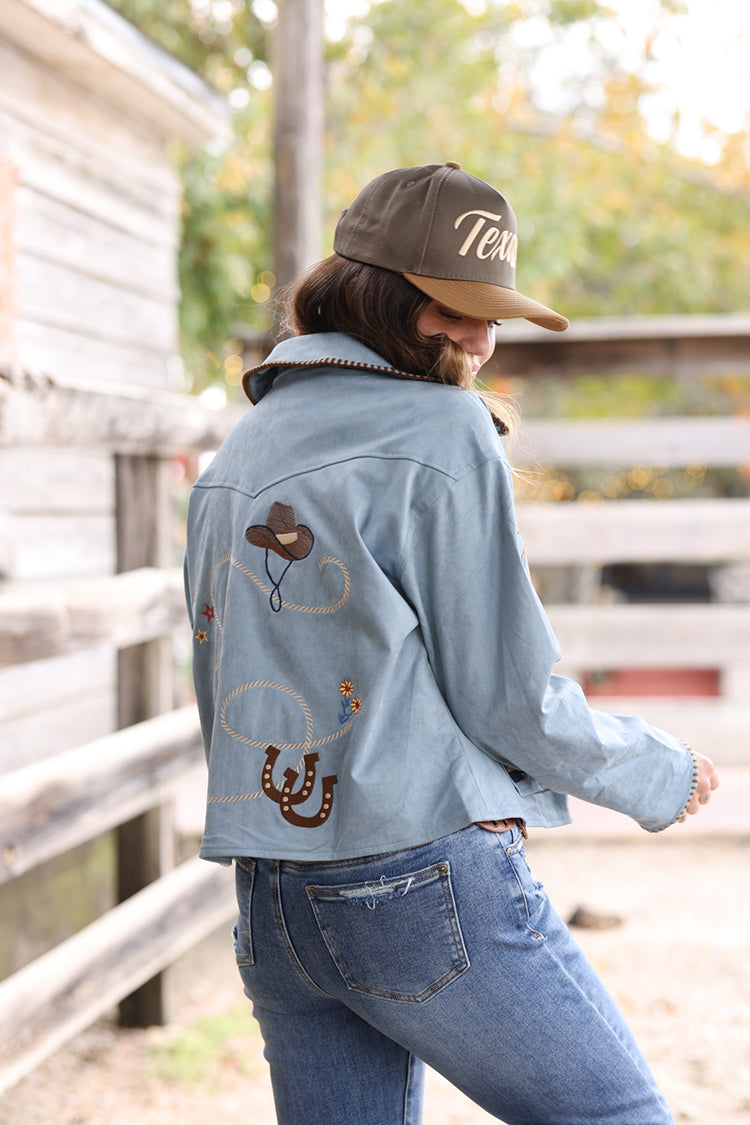 Woman wearing a light blue suede embroidered  jacket with patches, jeans, and a  Texas Embroidered Trucker Hat - Gold/Olive-FleaStyle