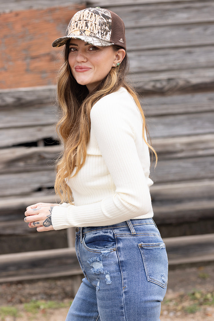 Woman wearing a Camouflage cap with 'Howdy Darlin'' text  white long-sleeve shirt with blue jeans -FleaStyle