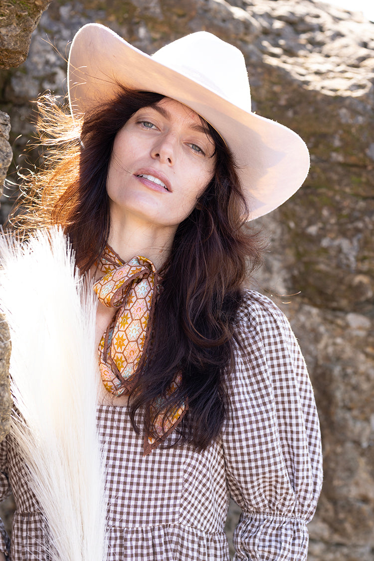 Woman wearing a Flea Style Rider Ivory Western Hat and checkered dress against rocks.