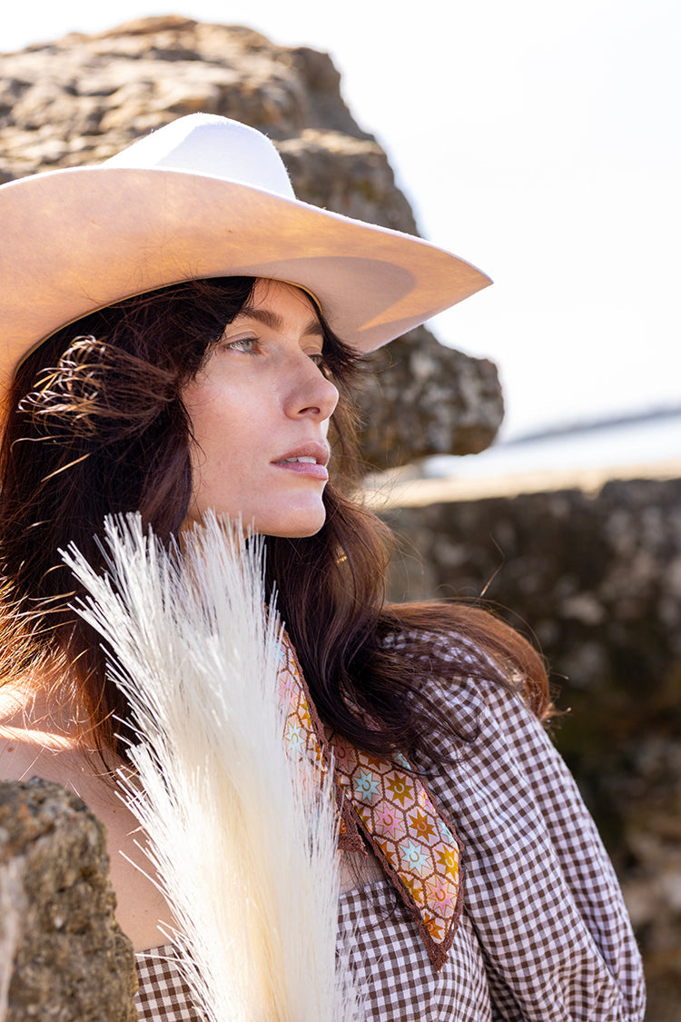 Woman wearing a Flea Style Rider Ivory Western Hat and checkered dress against rocks.