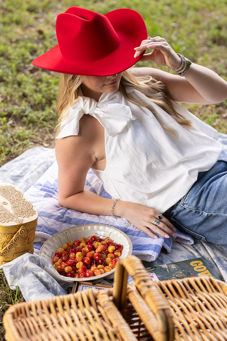Woman in a red hat sitting on a blanket with a picnic setup in a grassy area.